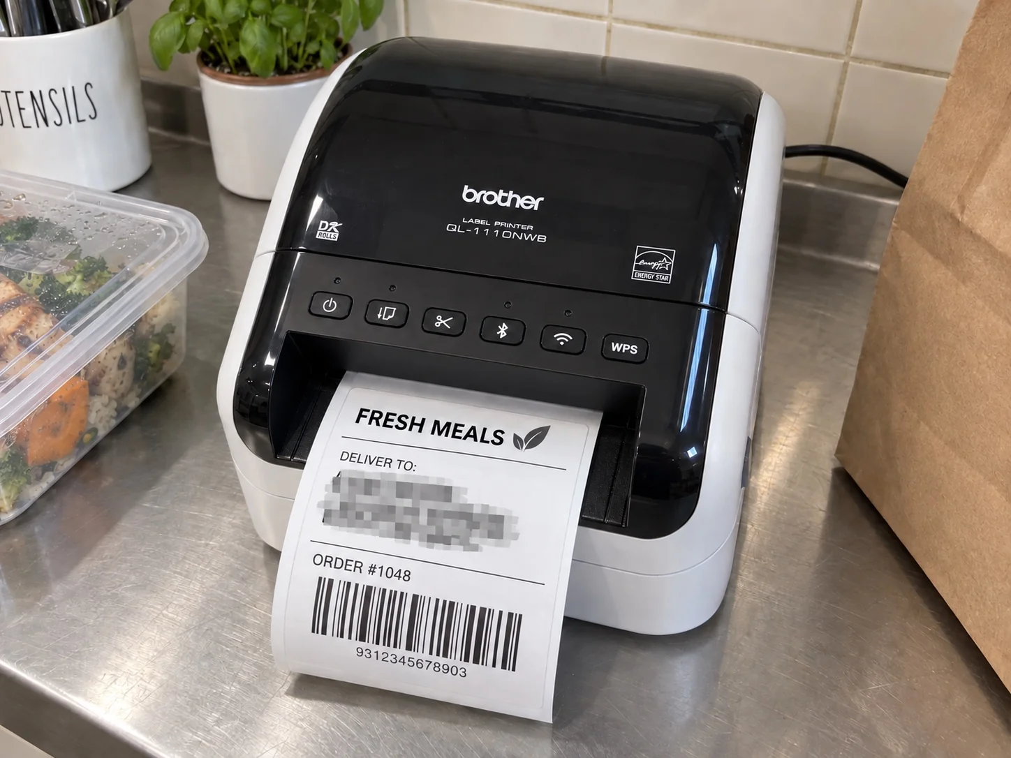 Brother thermal label printer producing a custom meal-delivery label on a stainless-steel kitchen bench.